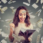 excited-woman-having-online-win-cheerful-table-happy-lottery-holding-fist-up-money-flying-around-118185733
